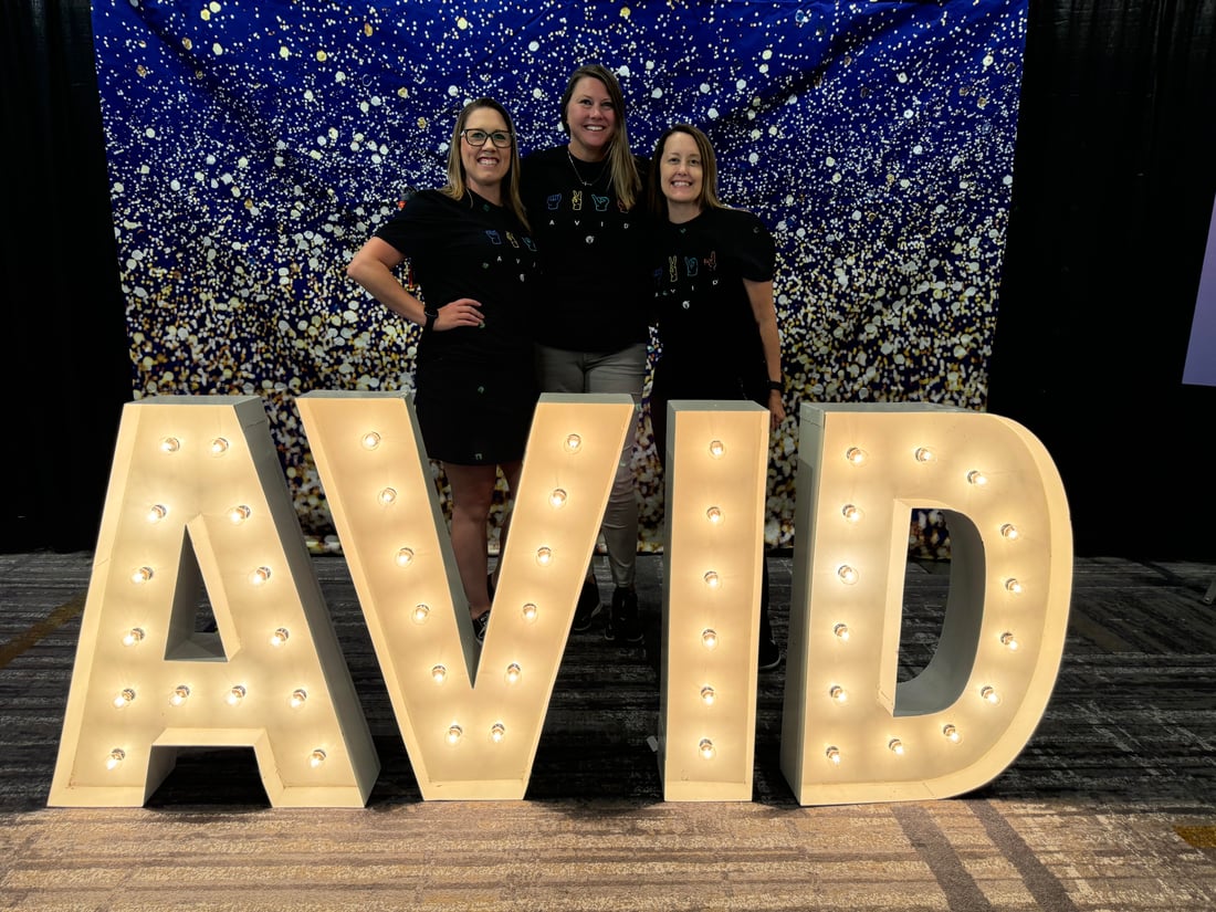 3 teachers standing behind a lit sign that says "AVID"