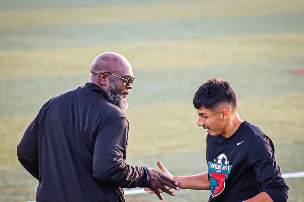 Wedlow and a student shake hands on a field